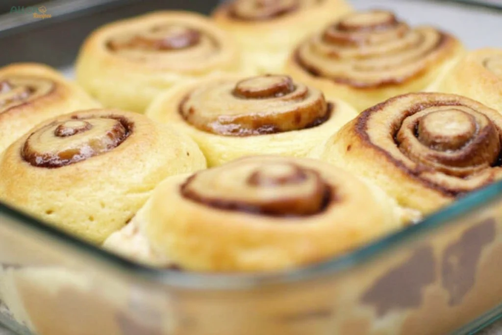 A golden sourdough discard cinnamon rolls glazed with icing, served on a white plate, with its spiral texture highlighted.